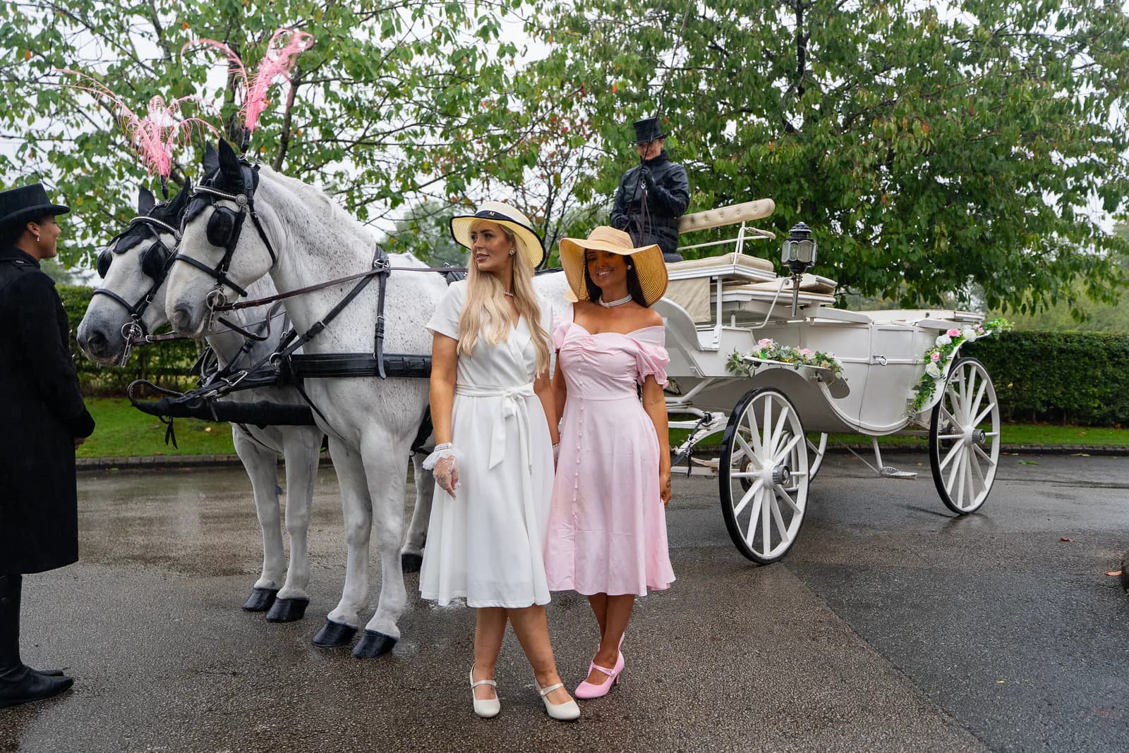 Two women from House of GirlBoss standing beside a white horse-drawn carriage.