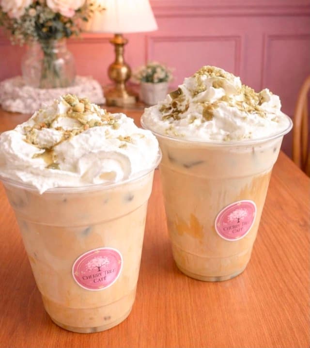 Two iced drinks topped with cream in Cherry Tree Cafe branded cups.